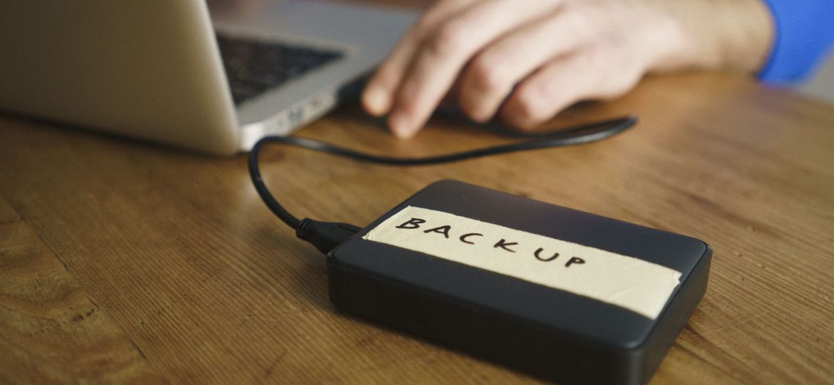 Midsection of man using laptop with backup label on external hard disk drive at table